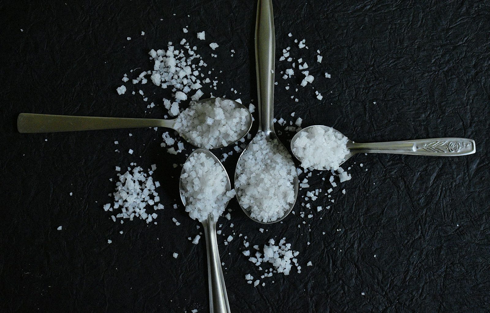 Fire skjeer fylt med salt arrangert på mørk overflate